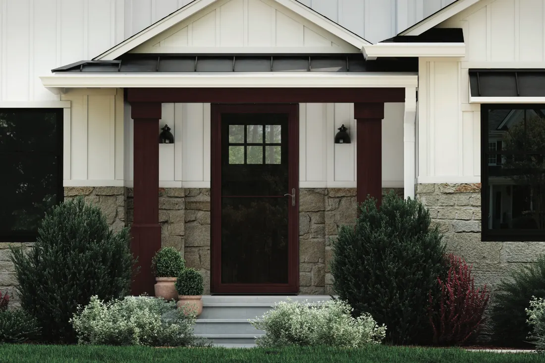 Dark red storm door on a covered front porch with stone and white siding