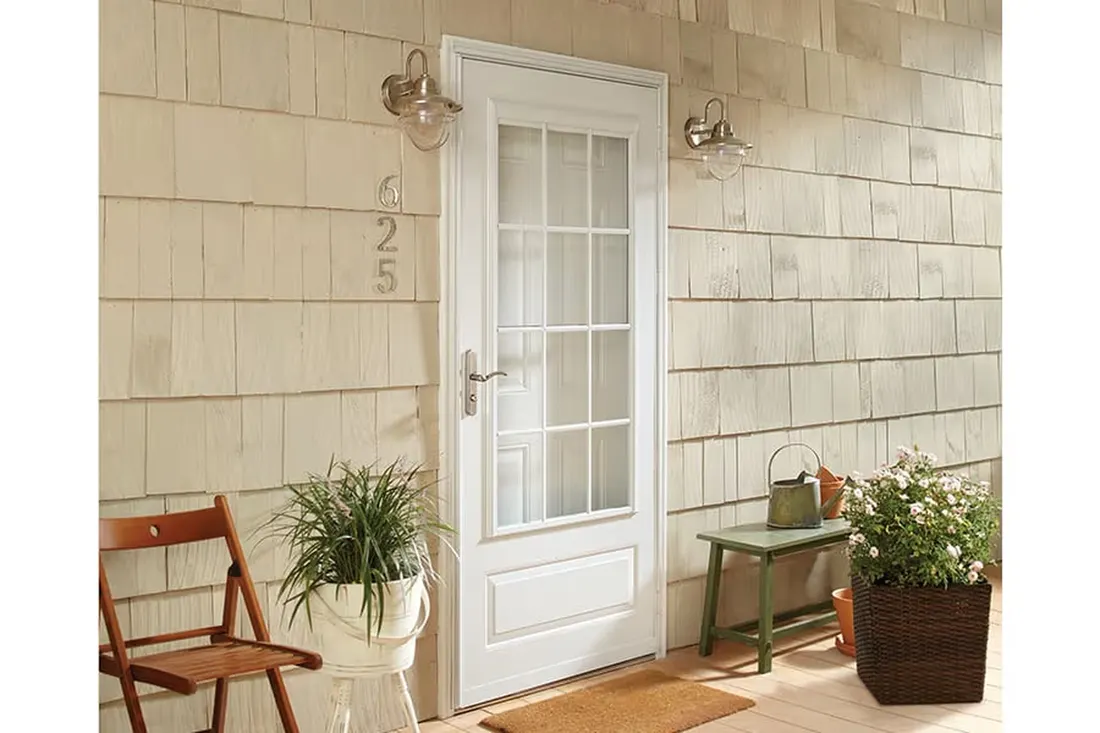 White multi-pane glass storm door installed on a tan shake-shingle house entryway with potted plants