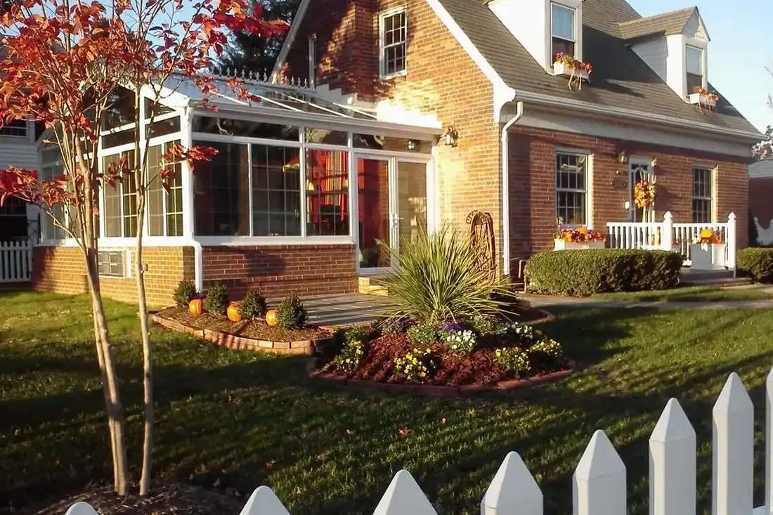 Gable sunroom addition on a red brick home with a picket fence