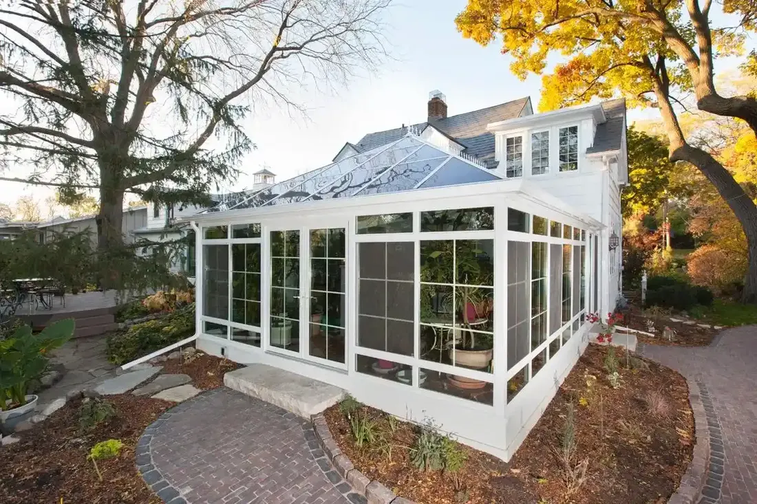 White glass sunroom addition with a gabled glass roof beside a brick garden path