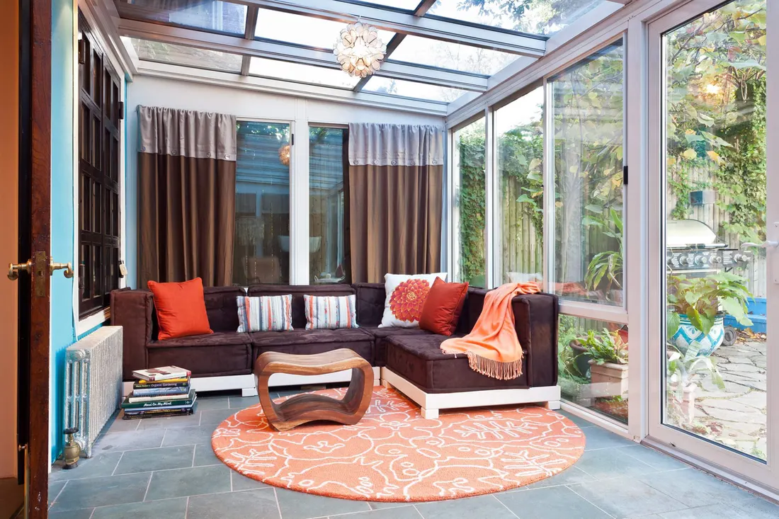 Glass-roof sunroom with a dark sectional and an orange rug