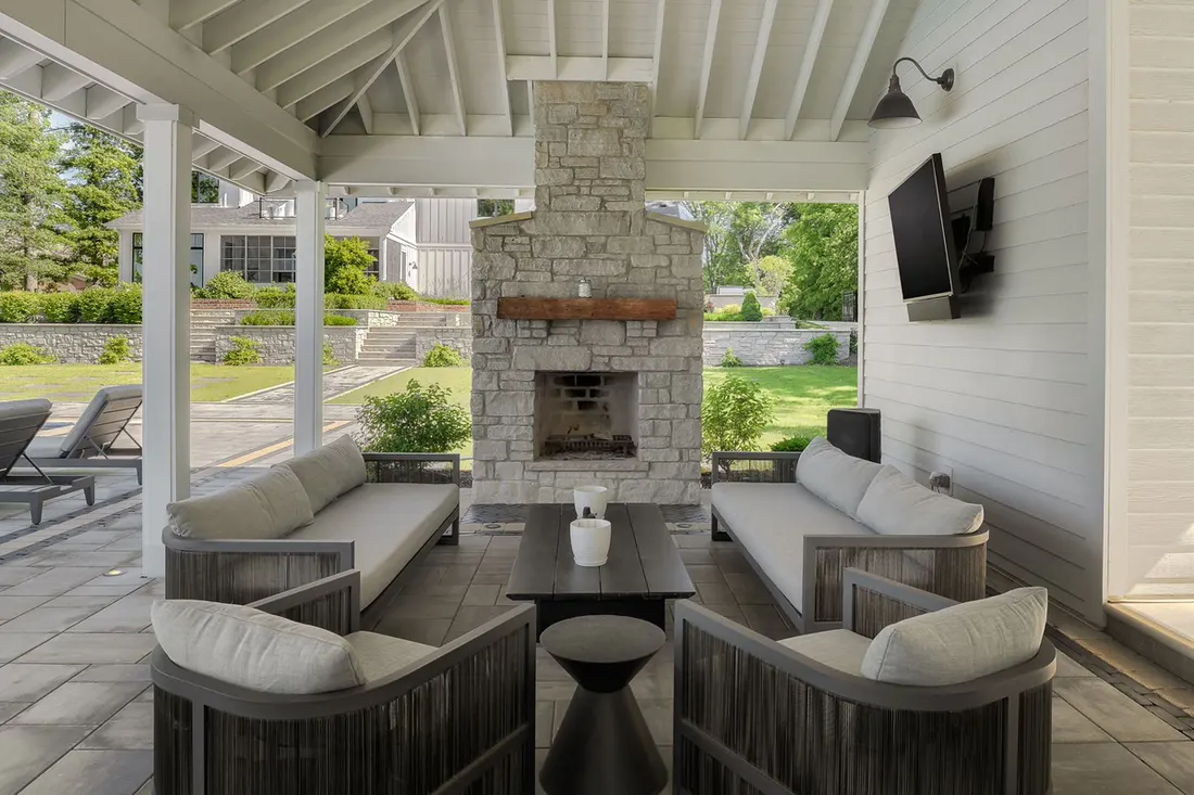 Covered patio with a stone fireplace, TV and gray outdoor sofas