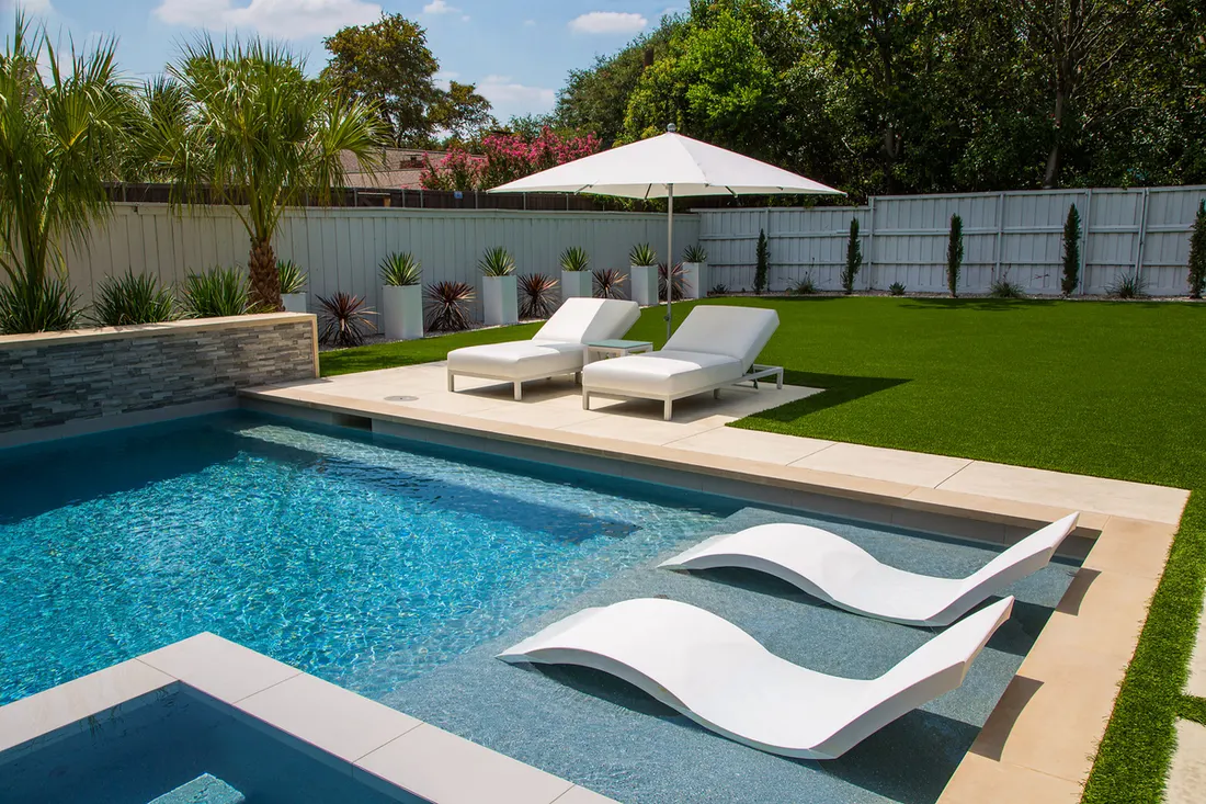 Pool with white in-water loungers, umbrella and lawn in a backyard