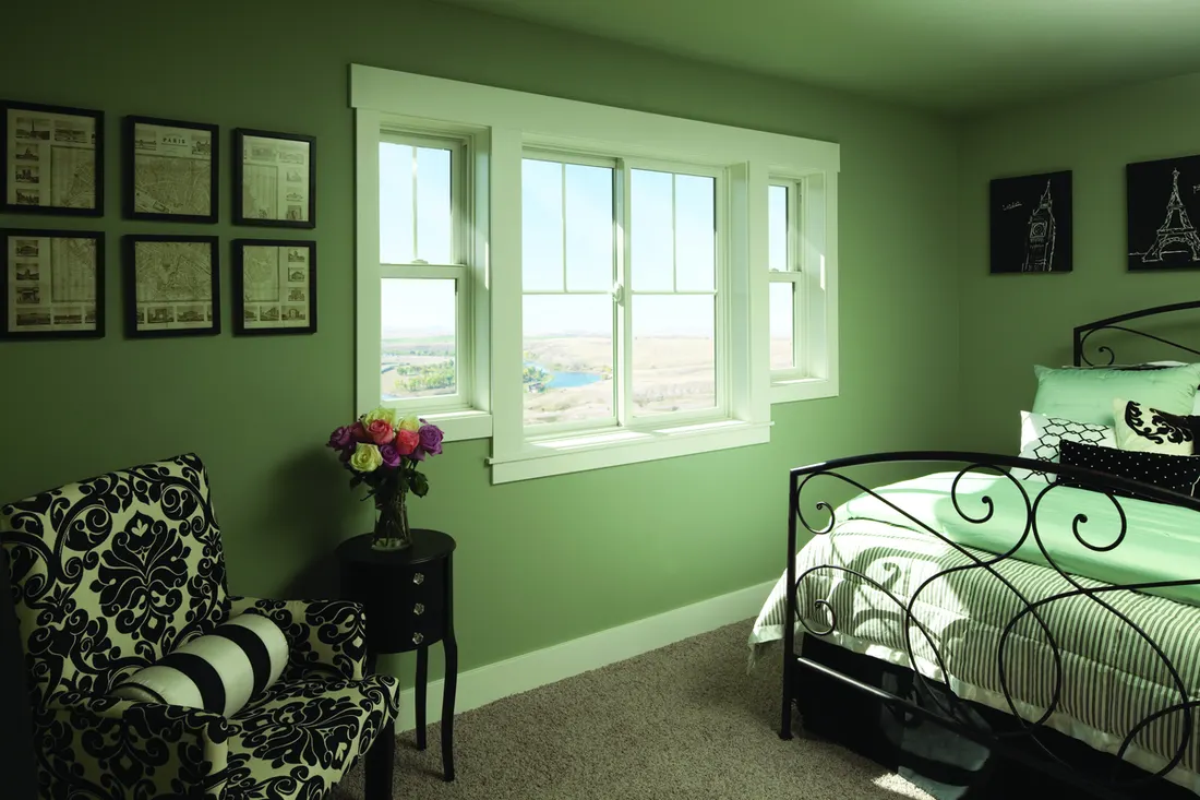 White-trimmed sliding and hung windows installed in a bedroom with green walls and carpet