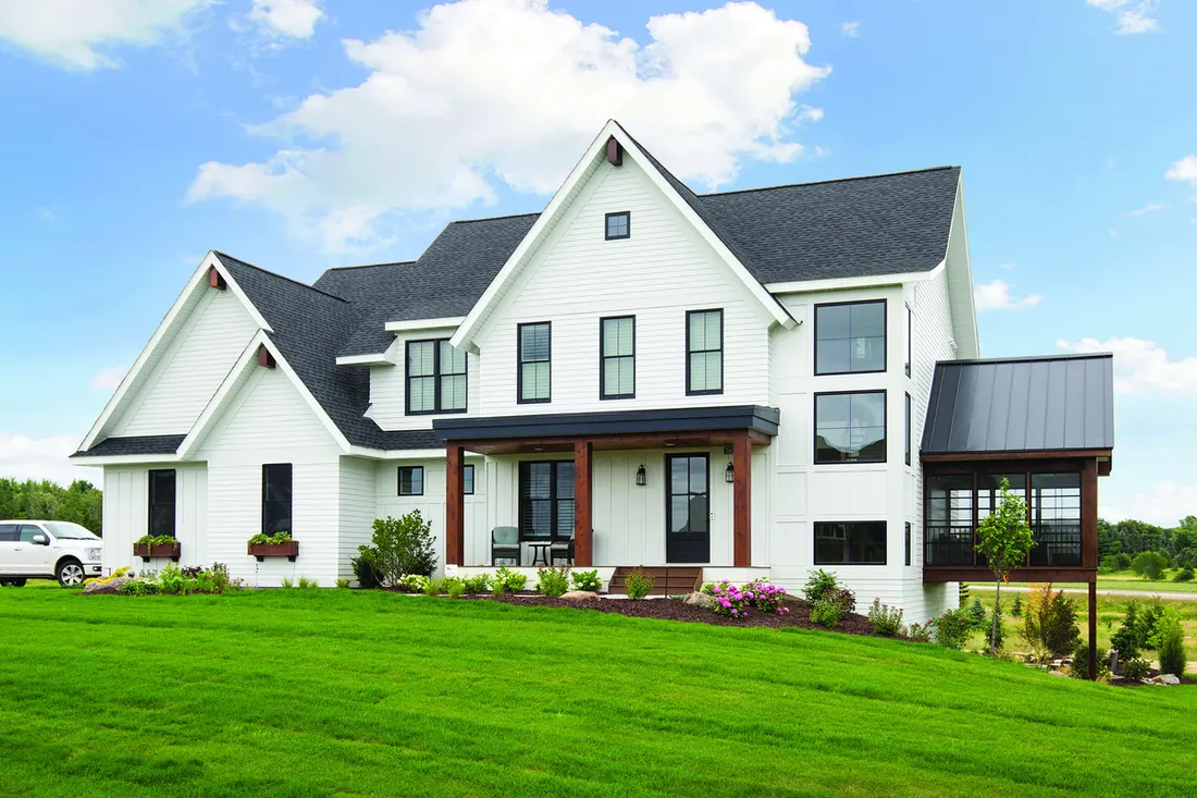 Modern two-story home with white siding, black framed windows, dark roof, and green lawn