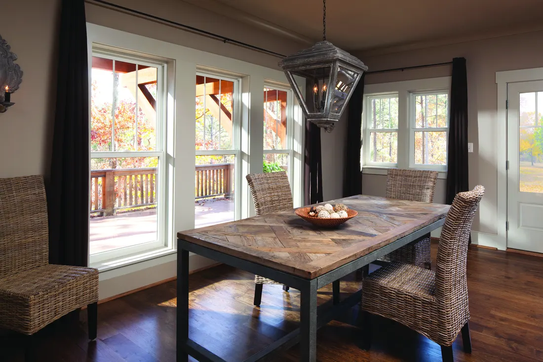 Dining room with large white-framed windows overlooking an outdoor wooden deck and trees
