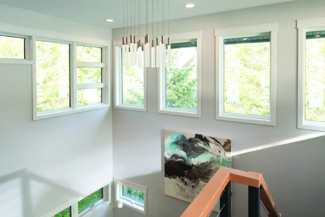 Multiple white-framed rectangular windows on grey walls in a high-ceiling stairwell with chandelier