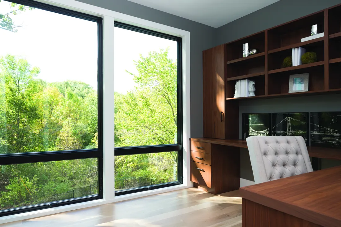 Large black-framed windows with white trim in a home office overlooking lush green trees