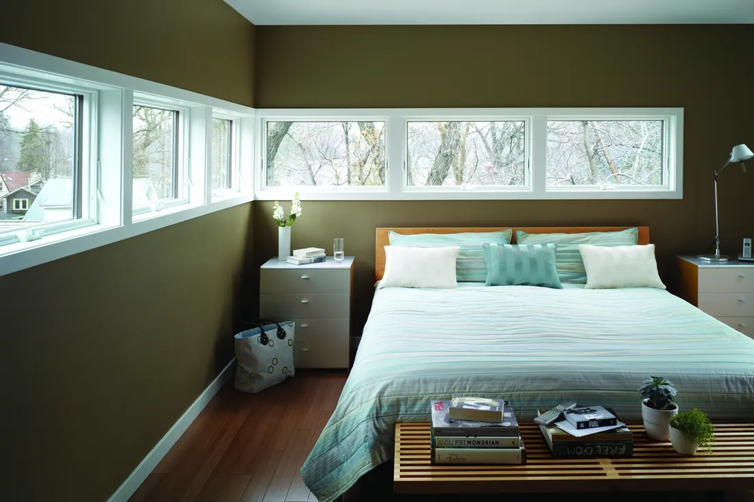 Corner ribbon windows with white trim in an olive-green bedroom above a modern bed