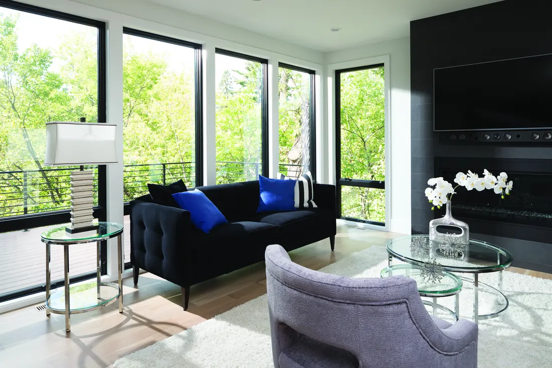 Large black-framed picture windows overlooking bright green trees in a contemporary living room