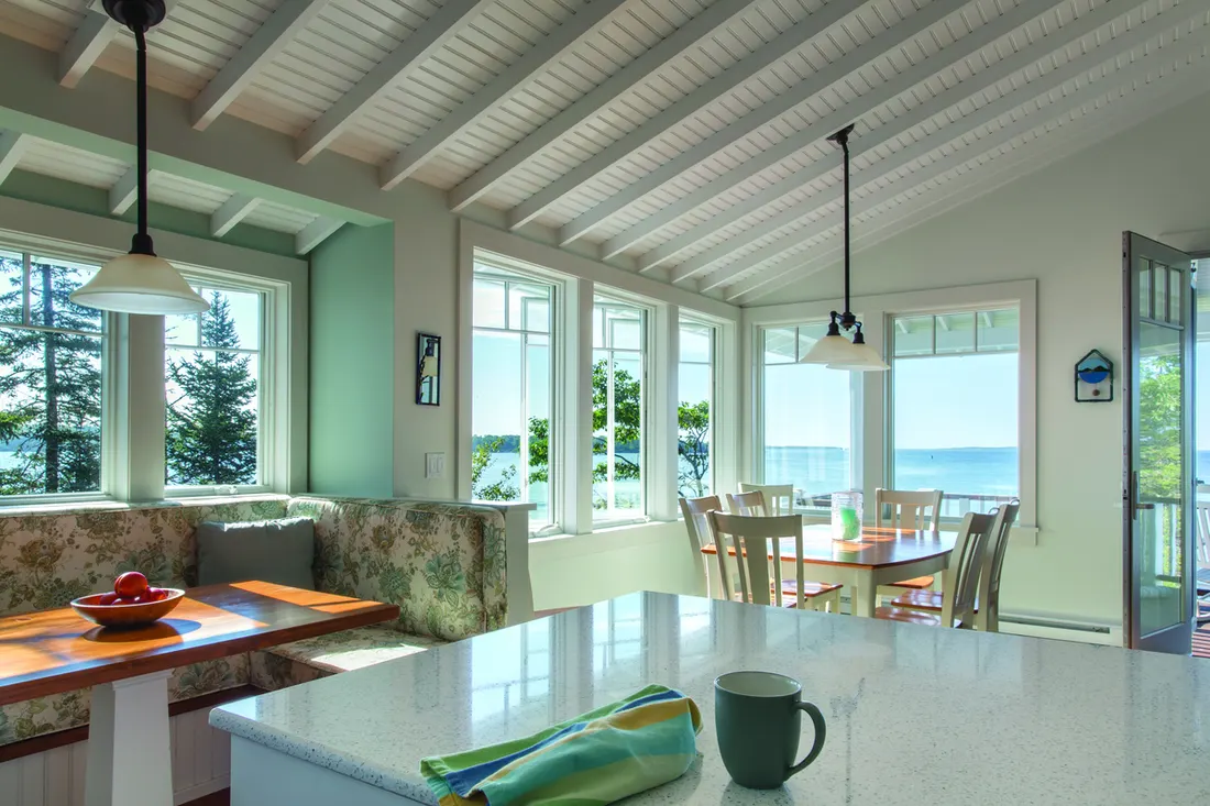 White casement windows overlooking water and trees in a bright dining area