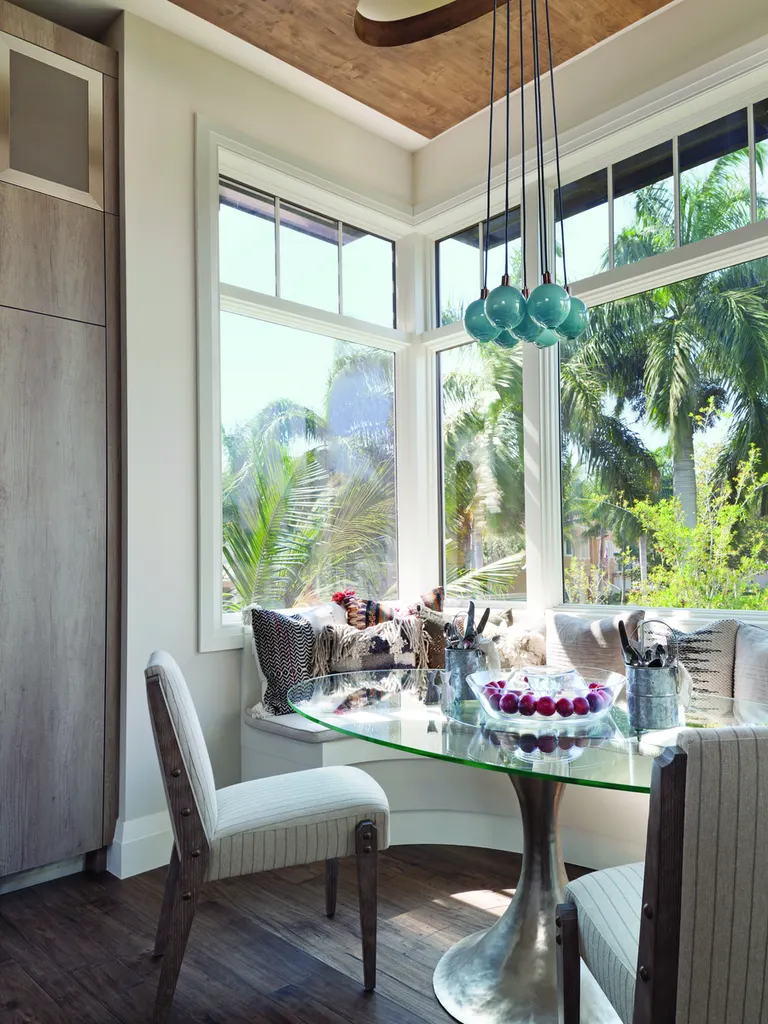 Large white-framed corner windows surrounding a breakfast nook with views of tropical palm trees