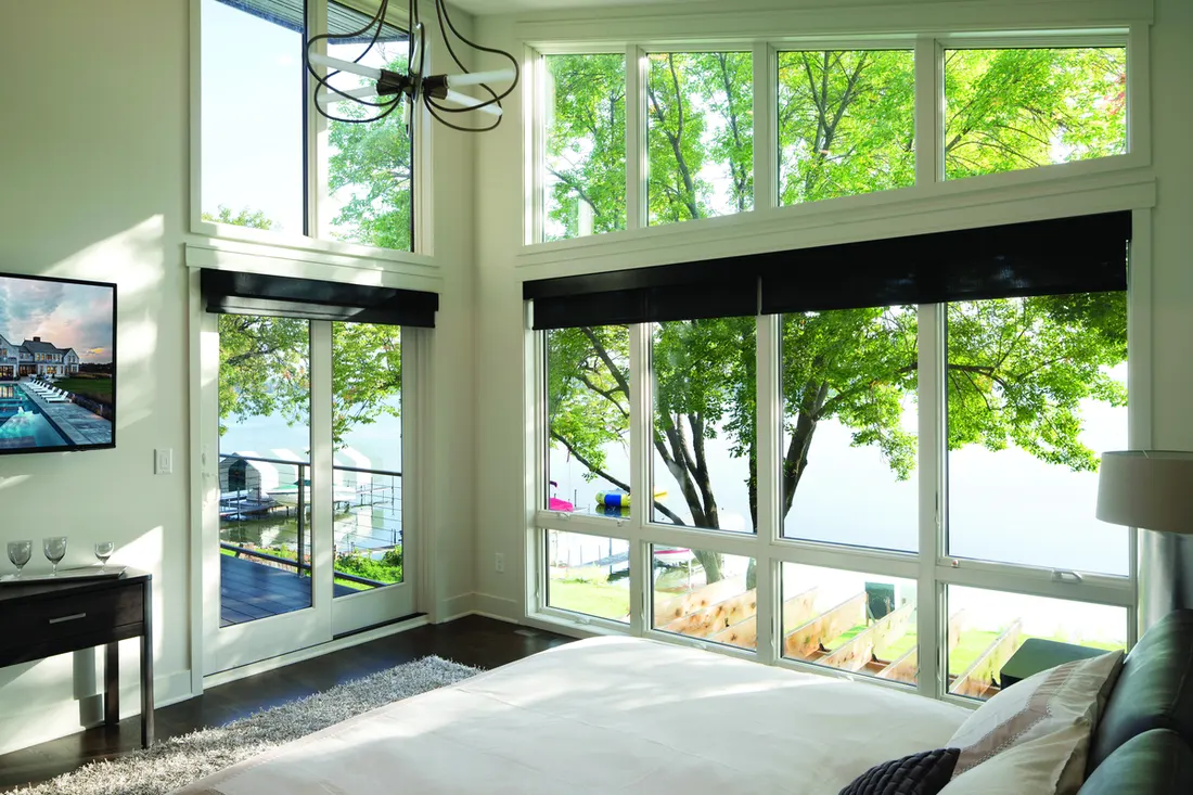 Multi-pane white windows and sliding glass door overlooking a scenic lake from a bedroom