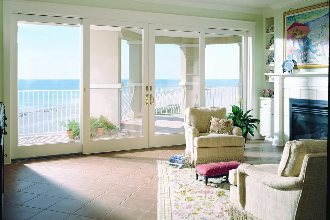 Large white-framed sliding glass doors and windows overlooking an ocean balcony in a sunlit living room