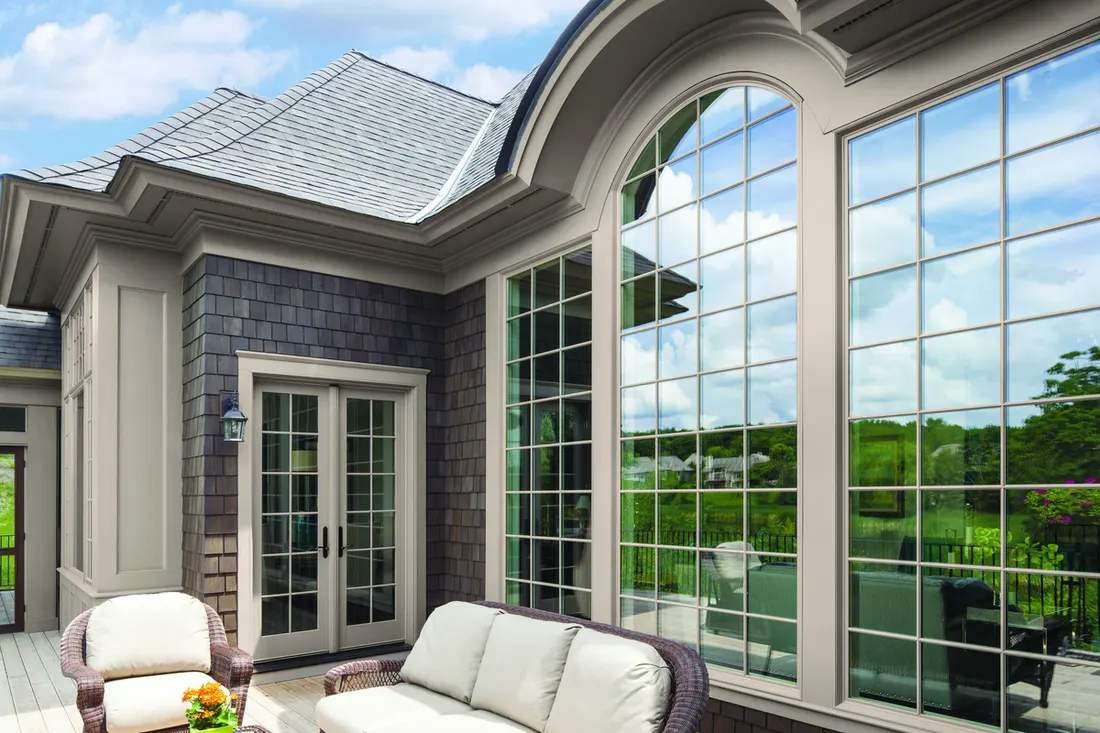 Large arched grid windows reflecting sky on a dark shingle home beside a patio
